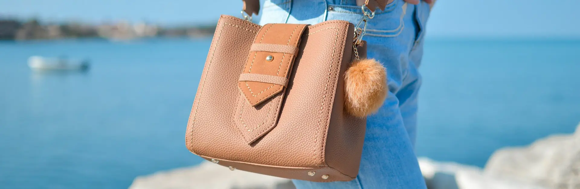 person hands on both pockets with crossbody bag near white rock